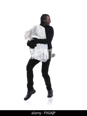 Thief in action carrying a big bag with balaclava on his face, dressed in black. Studio shot on white background. Stock Photo