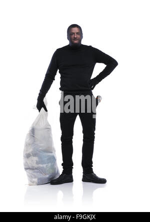 Thief in action carrying a big bag with balaclava on his face, dressed in black. Studio shot on white background. Stock Photo