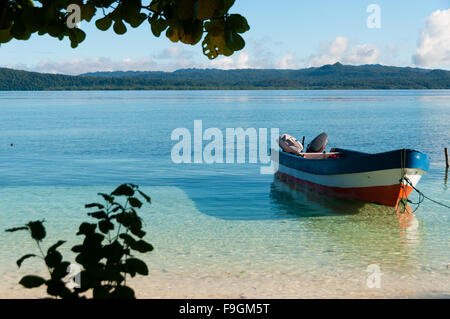 Small wooden boat in shallow clear water tied up by the white sand beach Stock Photo