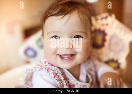 Cute little baby sitting in a high chair happy after being fed by her mother Stock Photo