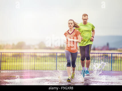 Young couple jogging on asphalt in rainy weather Stock Photo