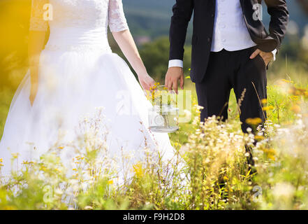 Unrecognizable young wedding couple holding hands as they enjoy romantic moments outside on a summer meadow Stock Photo