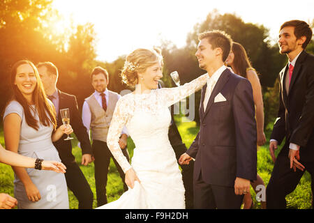 Full length portrait of newlywed couple dancing and having fun with bridesmaids and groomsmen in green sunny park Stock Photo