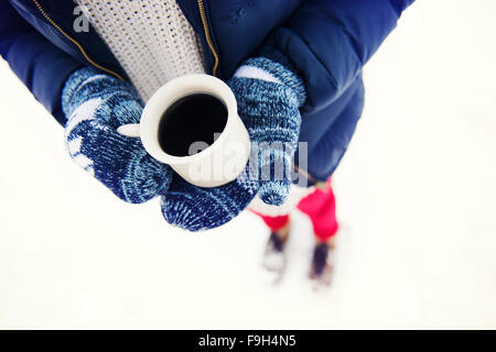 Hands of young woman holding a cup of coffee outside in snow