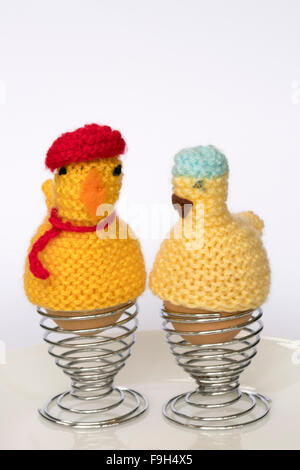 Two boiled eggs in egg cups with knitted funny  chicken egg cosies on them Stock Photo