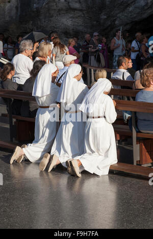 Nuns praying in the Grotto of Massabielle at the Sanctuary of Our Lady of Lourdes Stock Photo