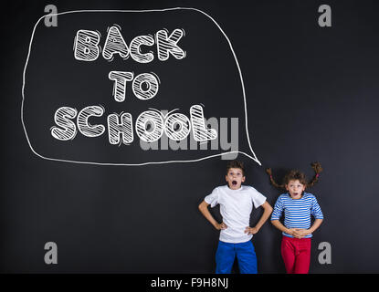 Cute boy and girl standing in frot of a big blackboard. Studio shot on black background. Stock Photo