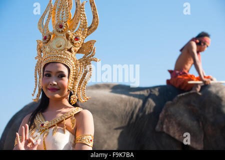 Traditional female Thai dancer stands in front of an elephant and mahout at the annual Surin Elephant Roundup on a blue sky day Stock Photo