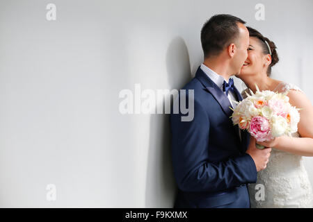 Beautiful bridal couple kissing next to white wall Stock Photo