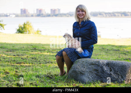 Woman sitting on rock holds little dog Stock Photo