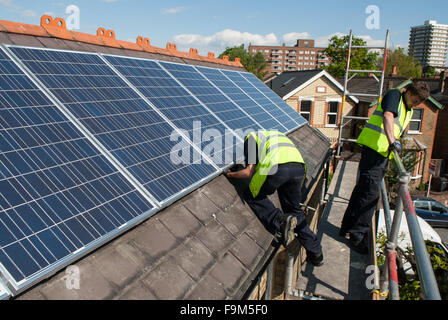 Workers install photovoltaic solar panels on the slate roof of a Victorian house in London, England. Stock Photo