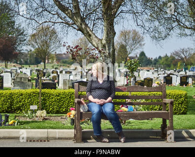 A grieving pregnant woman sitting on a bench in a graveyard or cemetery Stock Photo