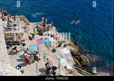 Sunbathers and swimmers at the bottom of the fortress wall, Dubrovnik, Croatia. Stock Photo