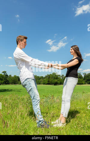 Young attractive caucasian couple holding each other in sunny green grass with blue sky Stock Photo