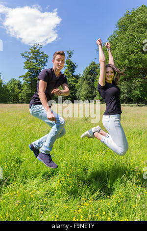 Young caucasian  man and woman  make jump in green grass on sunny day in summer Stock Photo