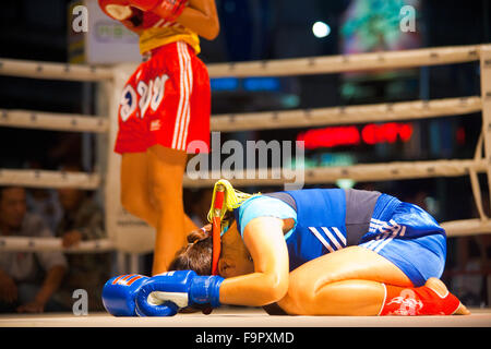 Female muay thai fighter in blue bowing her head on ring canvas performing a kickboxing ritual called the wai khru before match Stock Photo