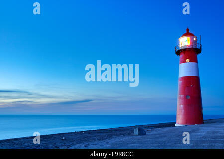 A red and white lighthouse at sea. Photographed at dusk near Westkapelle in Zeeland, The Netherlands. Stock Photo