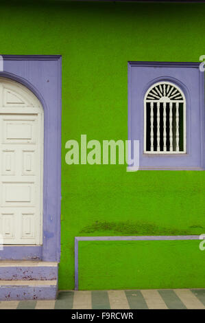 Green and purple stone wall of colonial house with white wooden closed door in Granada Stock Photo