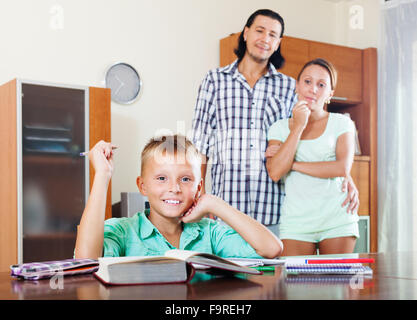 Happy  teenager schoolboy doing homework against  parents in home Stock Photo