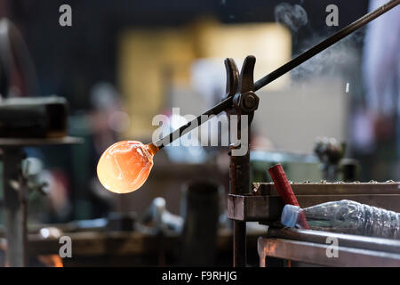 A piece of red hot melted glass is cooling down before further processing at a glassblowing factory/furnace. Stock Photo