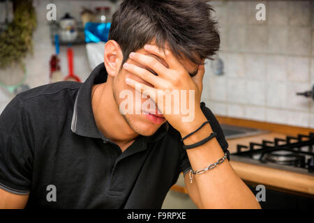 Depressed man hiding face with hand while sitting in the kitchen Stock Photo