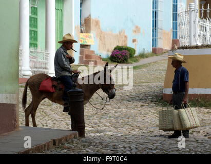 Man with cigar on donkey talking to man carrying bags, Trinidad, Cuba Stock Photo