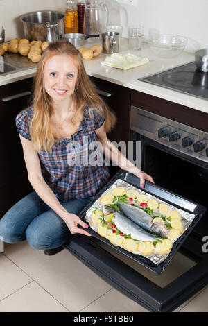 Long-haired girl cooking raw fish in oven at kitchen Stock Photo