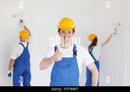 Smiling young builder in hardhat showing thumbs up indoors Stock Photo