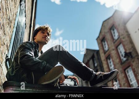 Ireland, Dublin, young man sitting on the ground of an alley Stock Photo