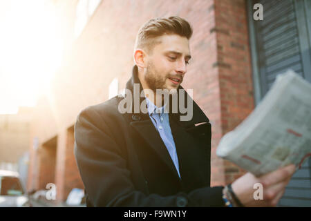 Young man walking on a street looking at newspaper Stock Photo