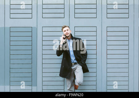 Young businessman leaning against facade telephoning with smartphone Stock Photo