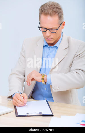 Businessman checking the time while doing paperwork. Stock Photo