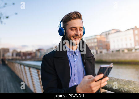 Ireland, Dublin, young man holding smartphone hearing music with headphones Stock Photo