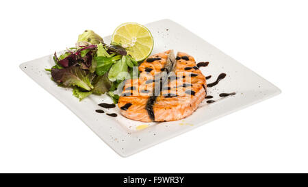 savory fish portion : roasted norwegian salmon fillet garnished with salad and basil leaves and lime on white dish isolated with Stock Photo