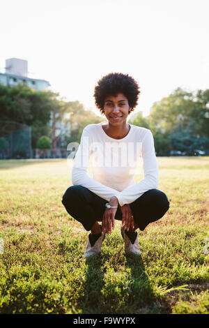 Portrait of smiling young woman crouching on a meadow at backlight Stock Photo