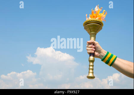 Hand of an athlete wearing Brazil colors sweatband holding sport torch against tropical blue sky Stock Photo