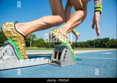 Athlete in gold shoes starting a race from the starting blocks on a blue running track Stock Photo