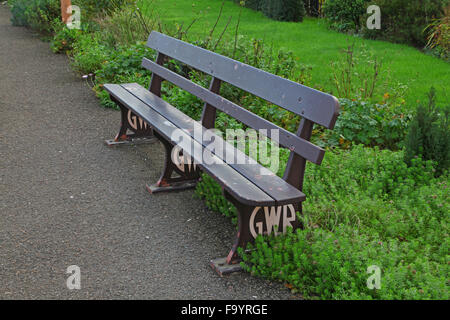 An old Great western station bench at the side of a platform with decorative cast Iron supports and wooden slats painted brown. Stock Photo