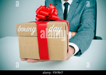 a young caucasian man in suit sitting at his office holding a gift tied with a red ribbon and the text boxing day Stock Photo