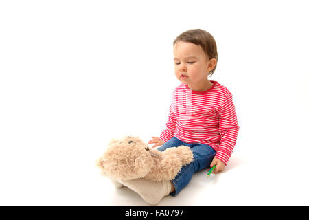 Sweet  toddler girl playing with her teddy bear putting him on feet to sleep Stock Photo