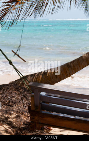 Wooden Bench Swing next to a palm tree in front of the caribbean white sand beach ocean on little corn island Stock Photo