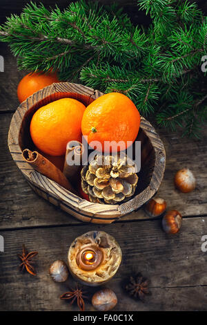 Wooden bucket with tangerines and pine cones on the background of Christmas trees Stock Photo