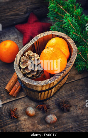 Wooden bucket with tangerines and pine cones on the background of Christmas trees and spices Stock Photo