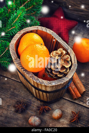 Wooden bucket with tangerines and pine cones on the background of Christmas trees and spices Stock Photo