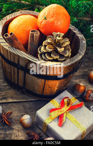 Wooden bucket with tangerines and pine cones on the background of Christmas trees and spices Stock Photo