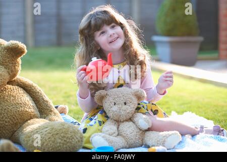 Girl having teddy bear picnic in garden holding toy teapot Stock Photo