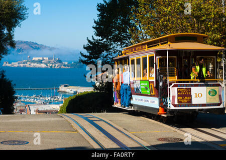 Powell Hyde cable car, an iconic tourist attraction, descending a steep hill peak overlooking Alcatraz prison island and the bay Stock Photo
