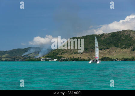 A tourist catamaran off the east coast of Mauritius, with sugarcane burning on the shore Stock Photo