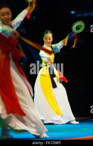 Two beautiful Korean women wearing colorful white hanbok dancing, playing traditional sogo drums on stage at a free outdoor show Stock Photo