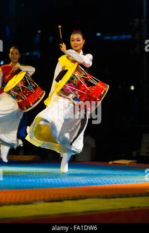 A young Korean woman in traditional hanbok jumping and playing the janggu drums at a free night summer show near city hall Stock Photo